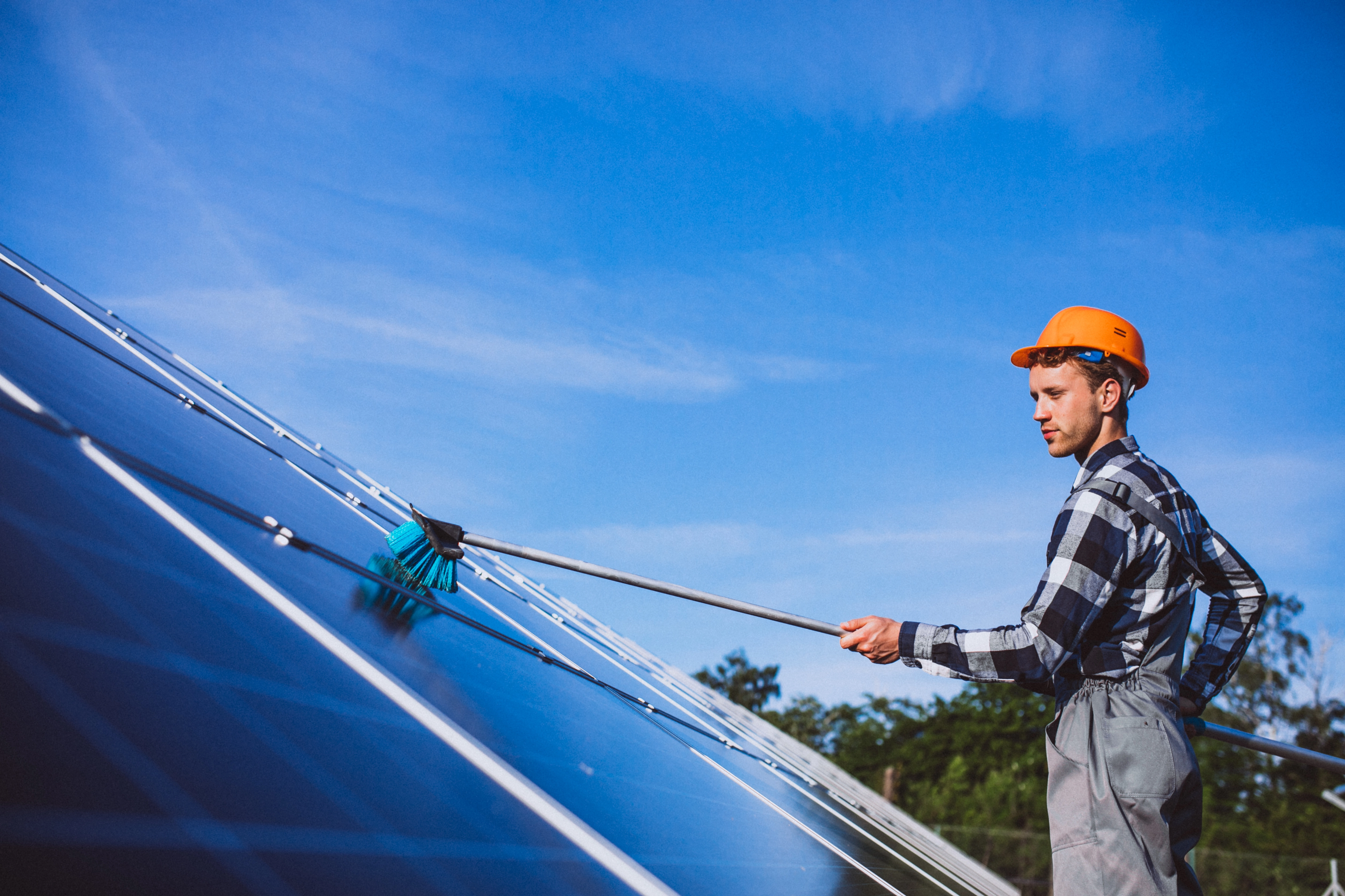 Un homme nettoyant des panneaux solaires sous un ciel bleu.